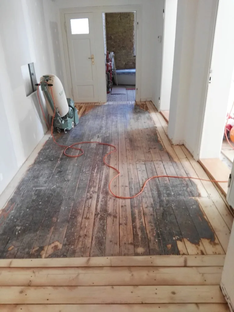Holzdielen im Flur während des Schliffs, mit Maschine und noch dunkler Altschicht