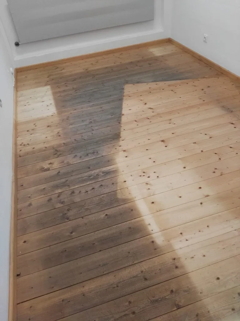 Holzdielen im Zimmer während des Schliffs, dunkle Altschicht neben hell geschliffener Fläche