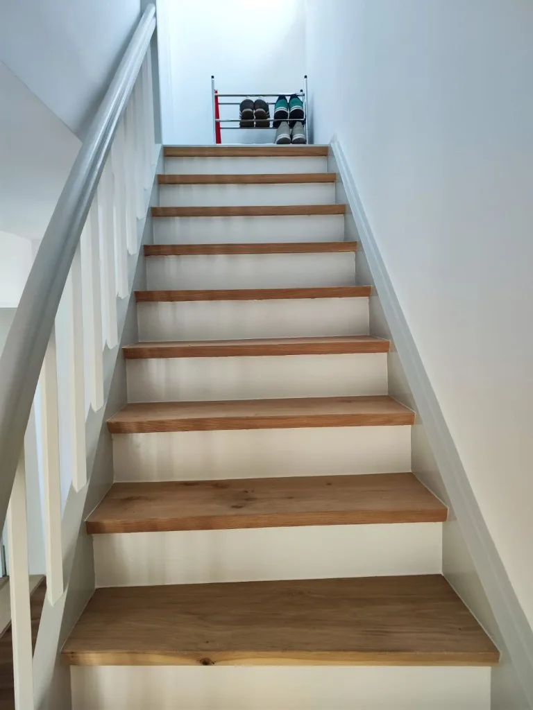 Renovierte Holztreppe von unten: Holzstufen, weiße Setzstufen und Wange