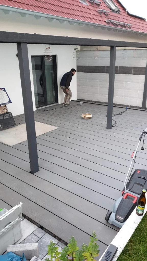 Fertige Terrasse mit grauem Dielenbelag an Hauswand und Pergola
